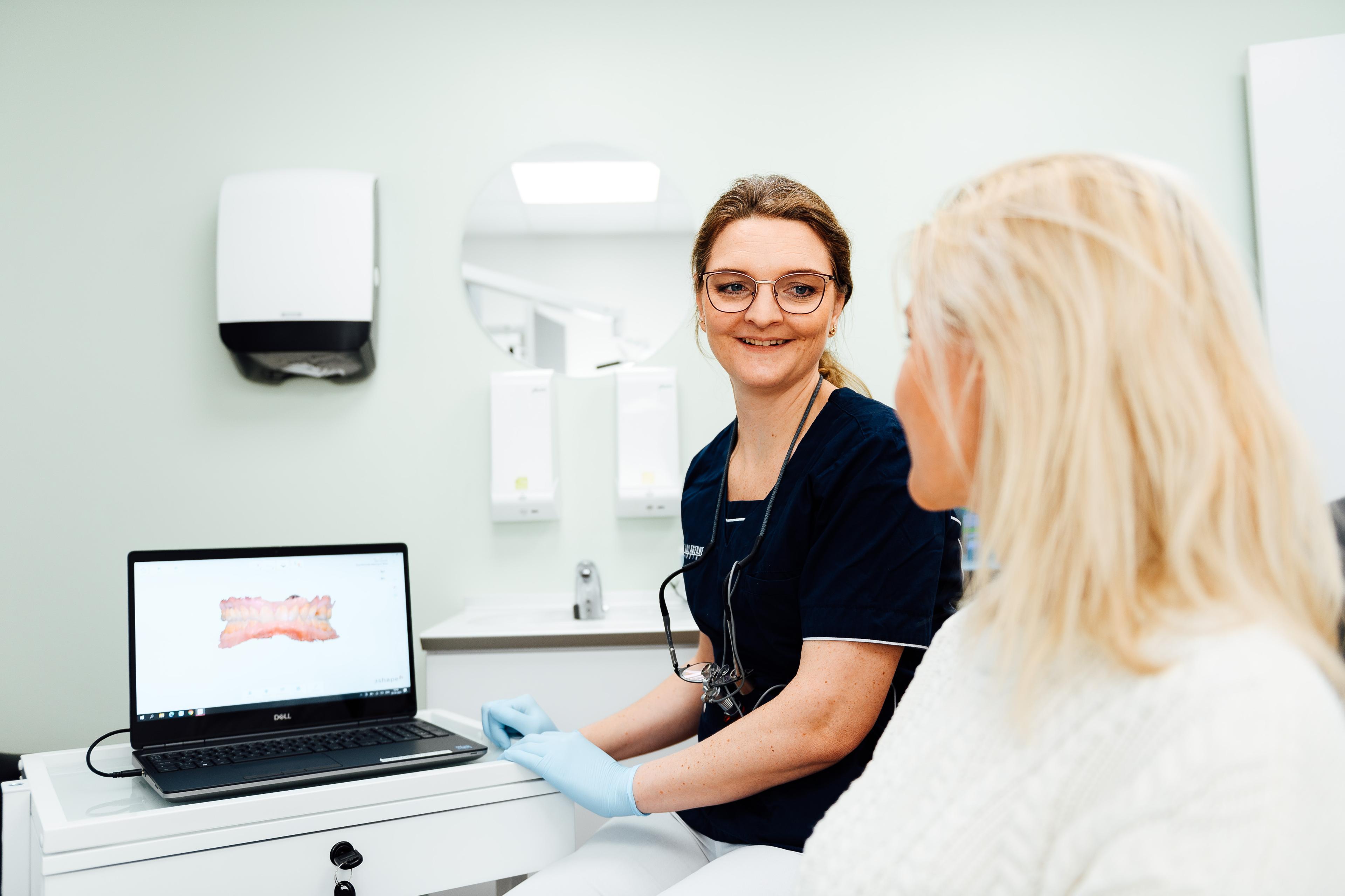 En tandlæge smiler til en patient, mens de ser på en tandbehandling på en bærbar computer.