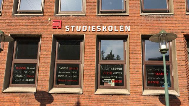 Facade af Studieskolen med vinduer og skilt, der viser sprogkurser i dansk og andre sprog.