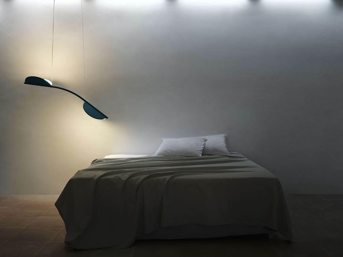 Et minimalistisk soveværelse med en seng, lys og en moderne lampe hængende fra loftet.