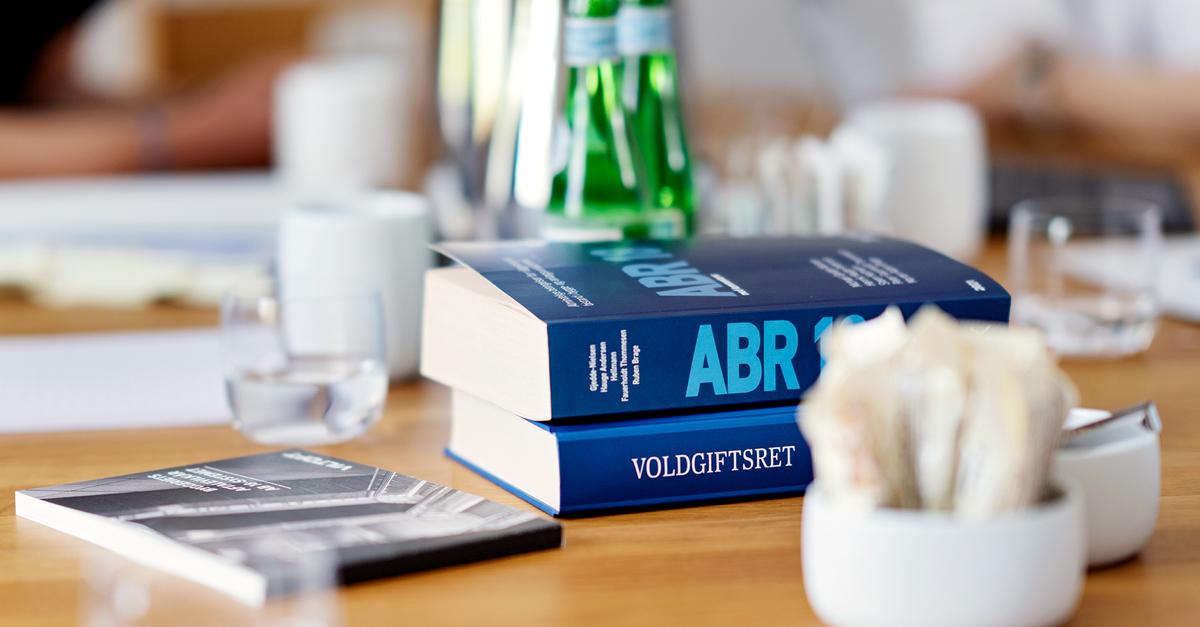 To bøger med titlerne "ABR" og "Værdighed" ligger på et bord med vandflasker og glas.