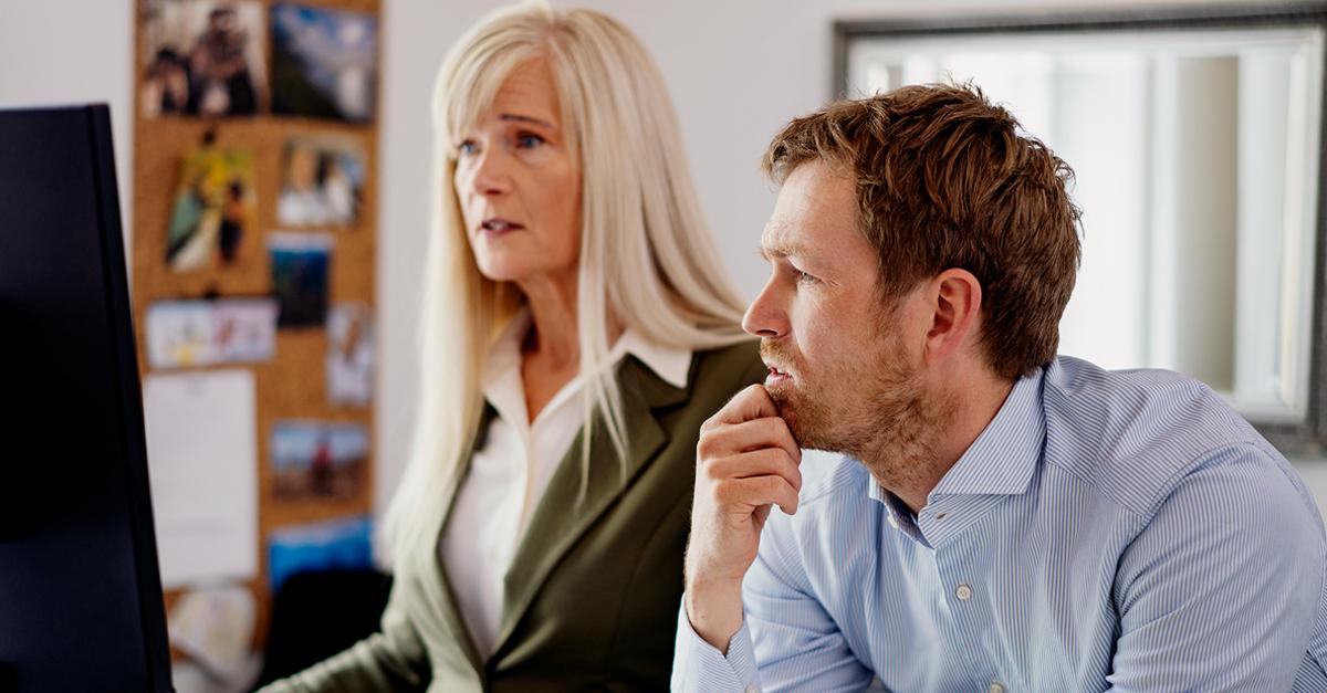 To personer, en mand og en kvinde, ser koncentreret på en computerskærm i et kontormiljø.