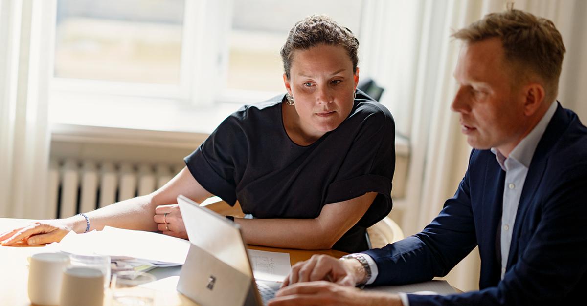 To personer, en mand og en kvinde, sidder ved et bord og diskuterer over en bærbar computer.