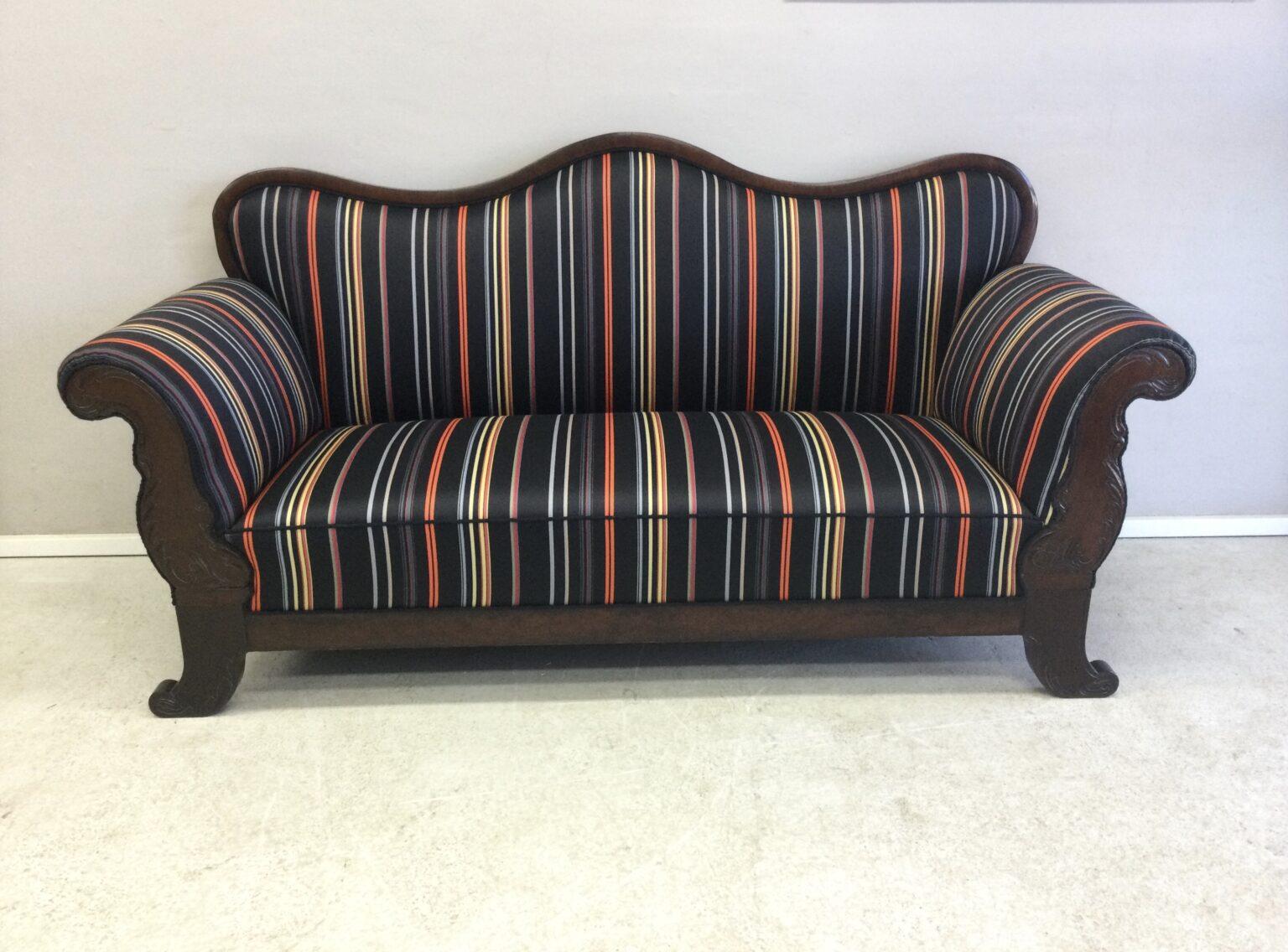 En farverig stribet sofa med træramme og buet ryg, placeret på en lys gulvflade.