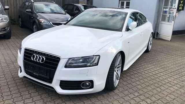 En hvid Audi S5 parkeret på en grusvej med andre biler i baggrunden.