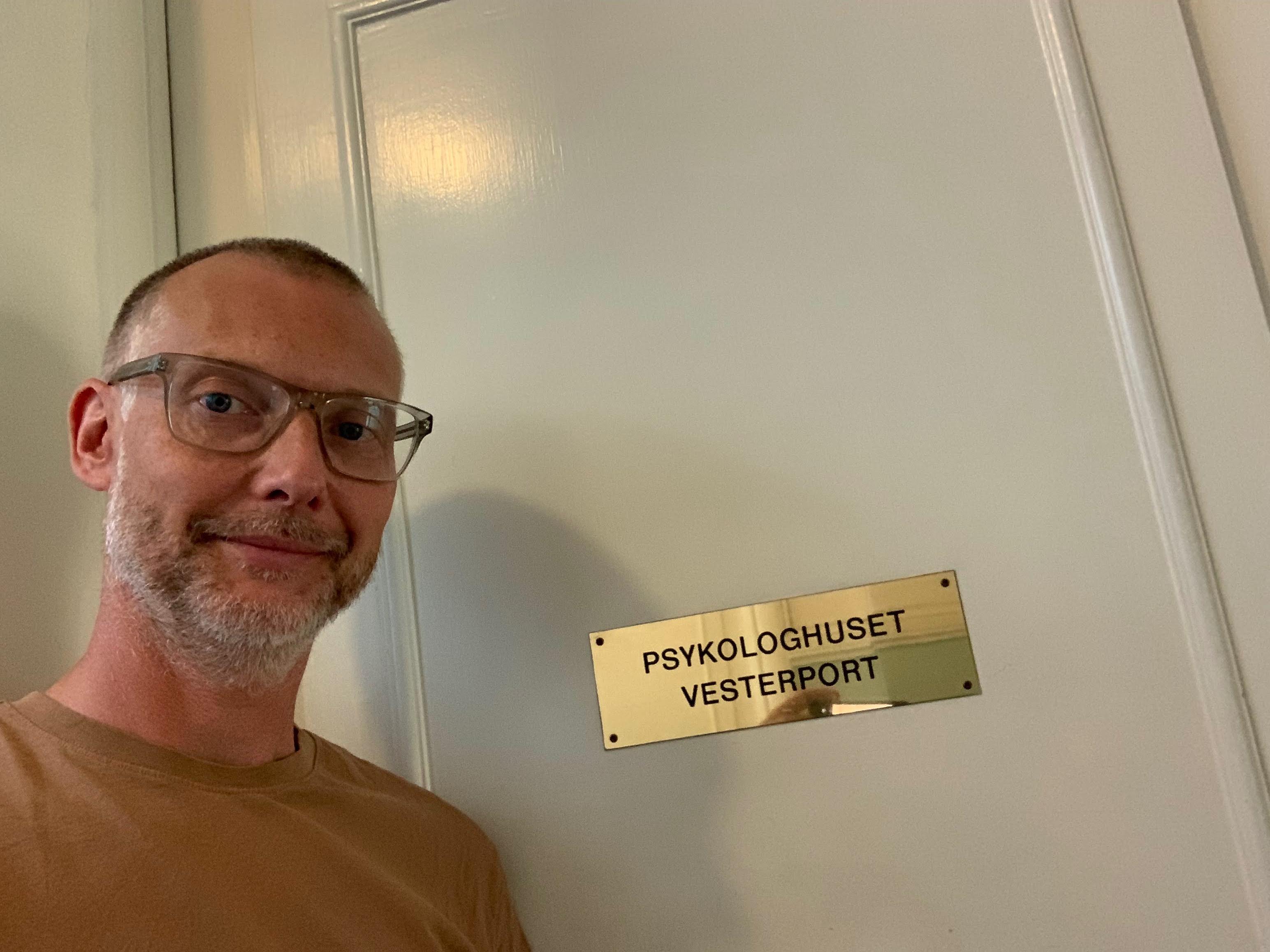 Mand står ved en dør med skiltet "Psykologhuset Vesterport" i en indendørs korridor.