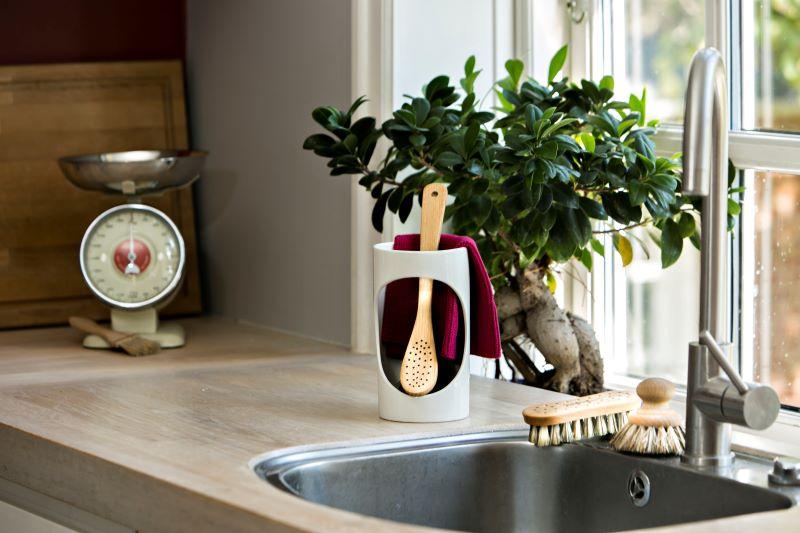 Køkkenbord med en skål, køkkenredskaber i en holder, en plante og en vægt i baggrunden.