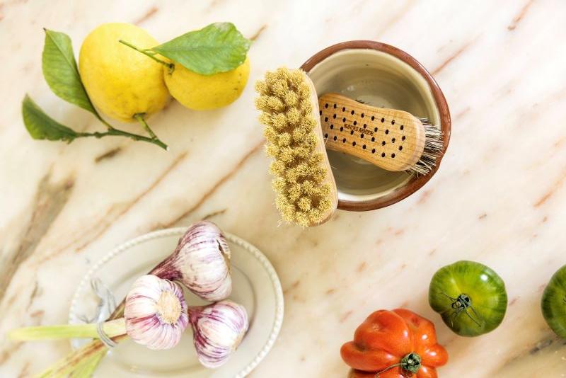 Friske grøntsager og citroner på et marmorbord med en børste og en skål i midten.