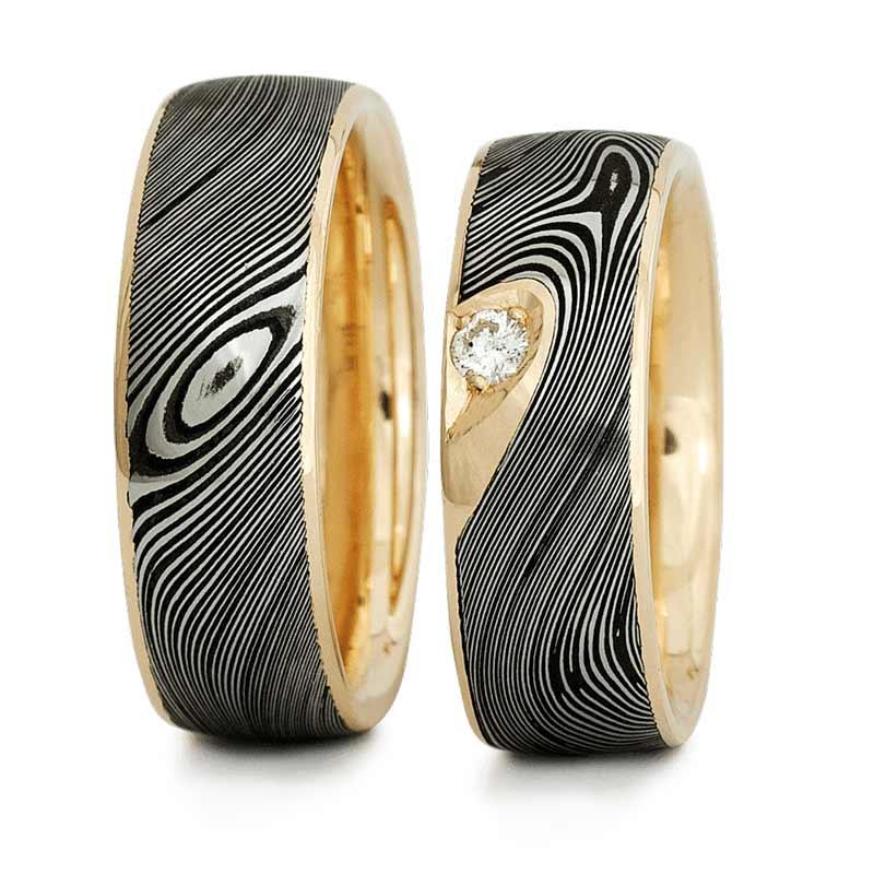 To smukke vielsesringe i guld med sort mønster og en diamant i den ene ring.