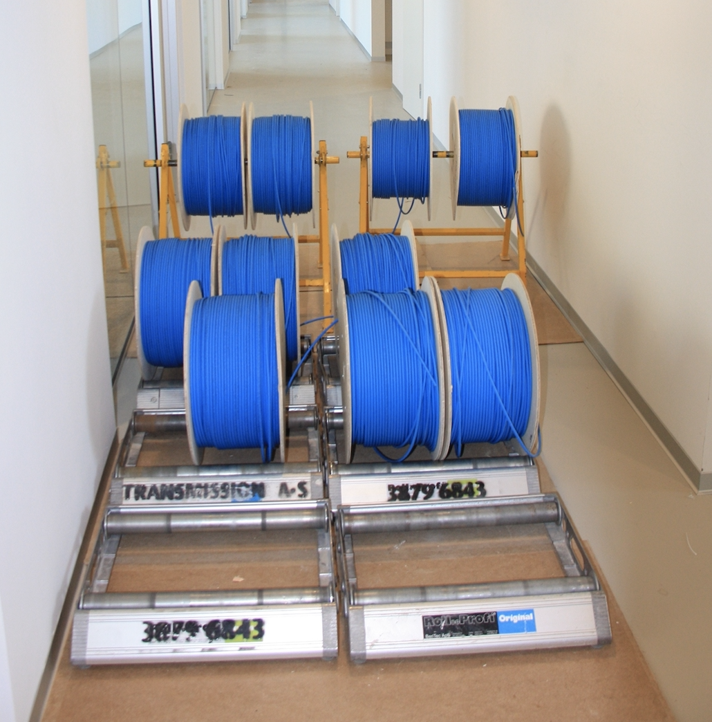 Blå kabler på ruller i en gang, organiseret på metalstativer, med labels på rullerne.