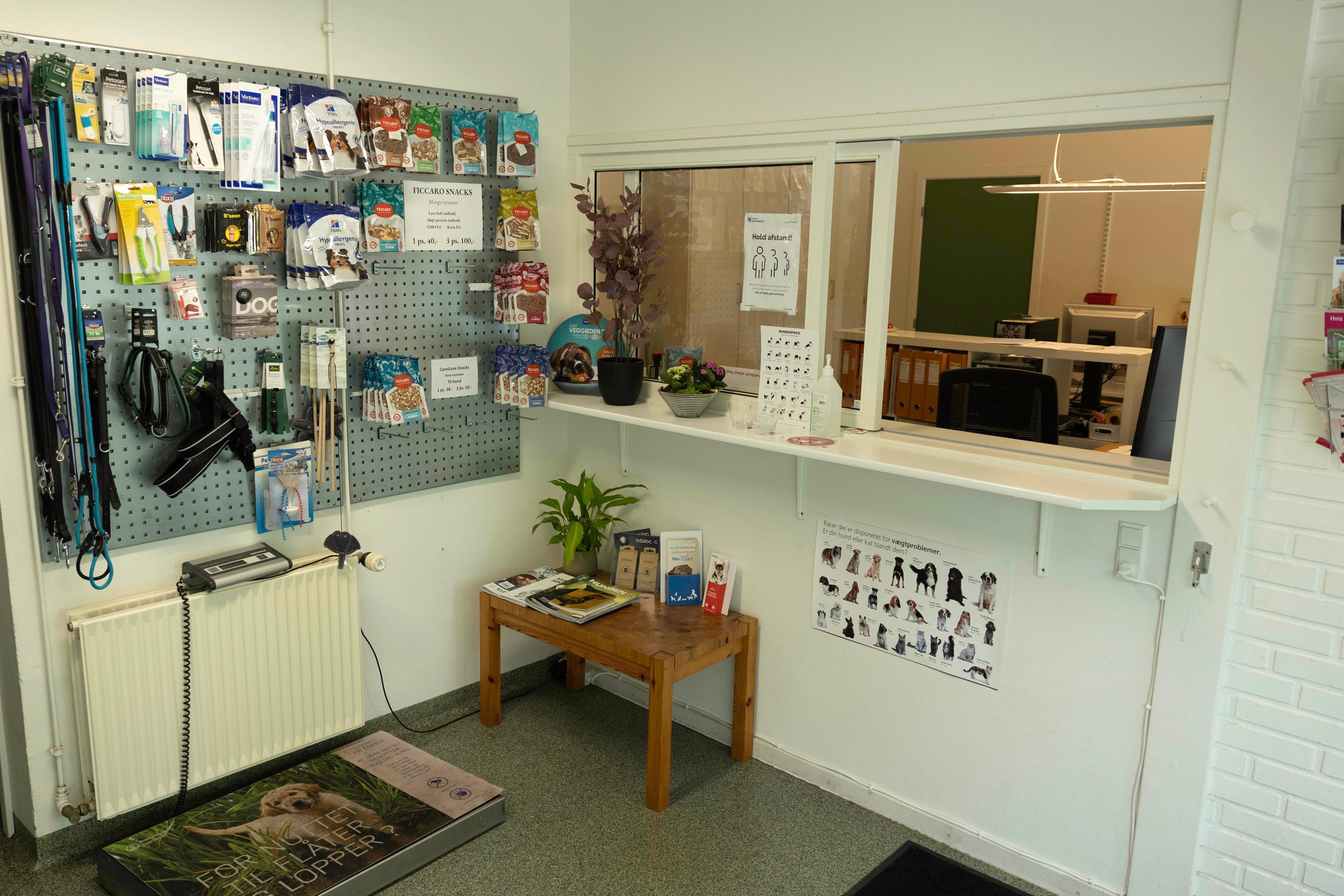 Indgang til en dyreklinik med hundesnore, plejeprodukter og en reception med planter og informationsmateriale.