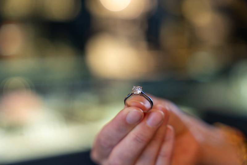 En person holder en smuk forlovelsesring med en diamant i hånden, mens de står i en smykkebutik.