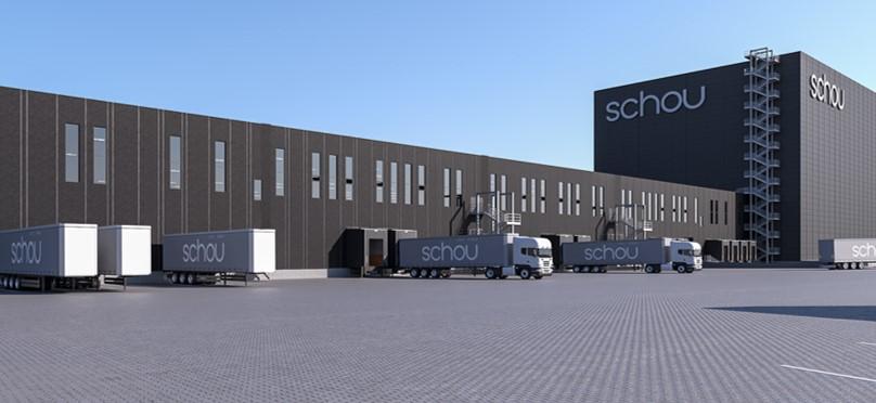 Moderne lagerbygning med lastbiler og containere parkeret foran, mærket med "schou".