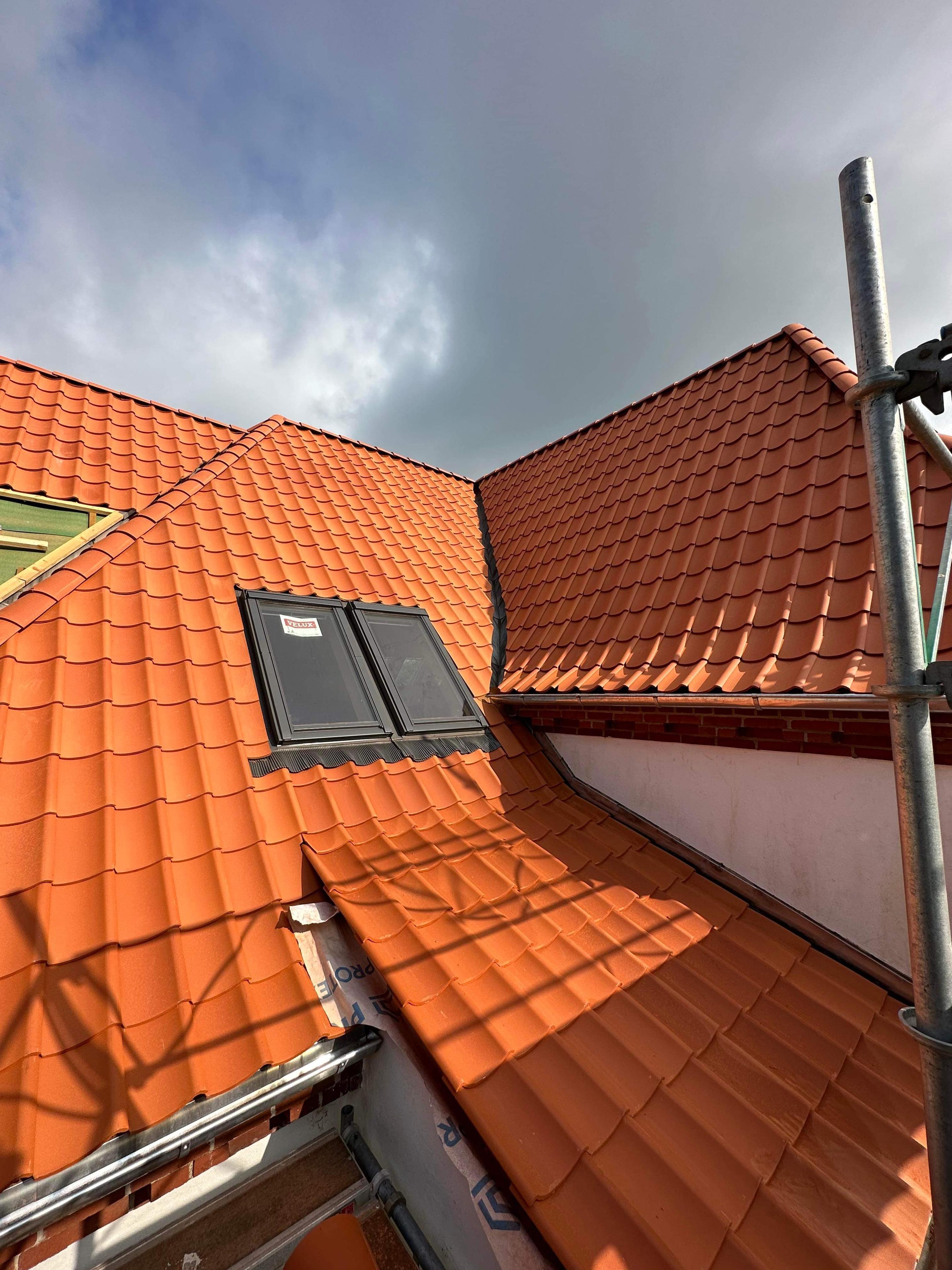 Tag med røde teglsten og vinduer under renovering, set fra en stilladsposition.