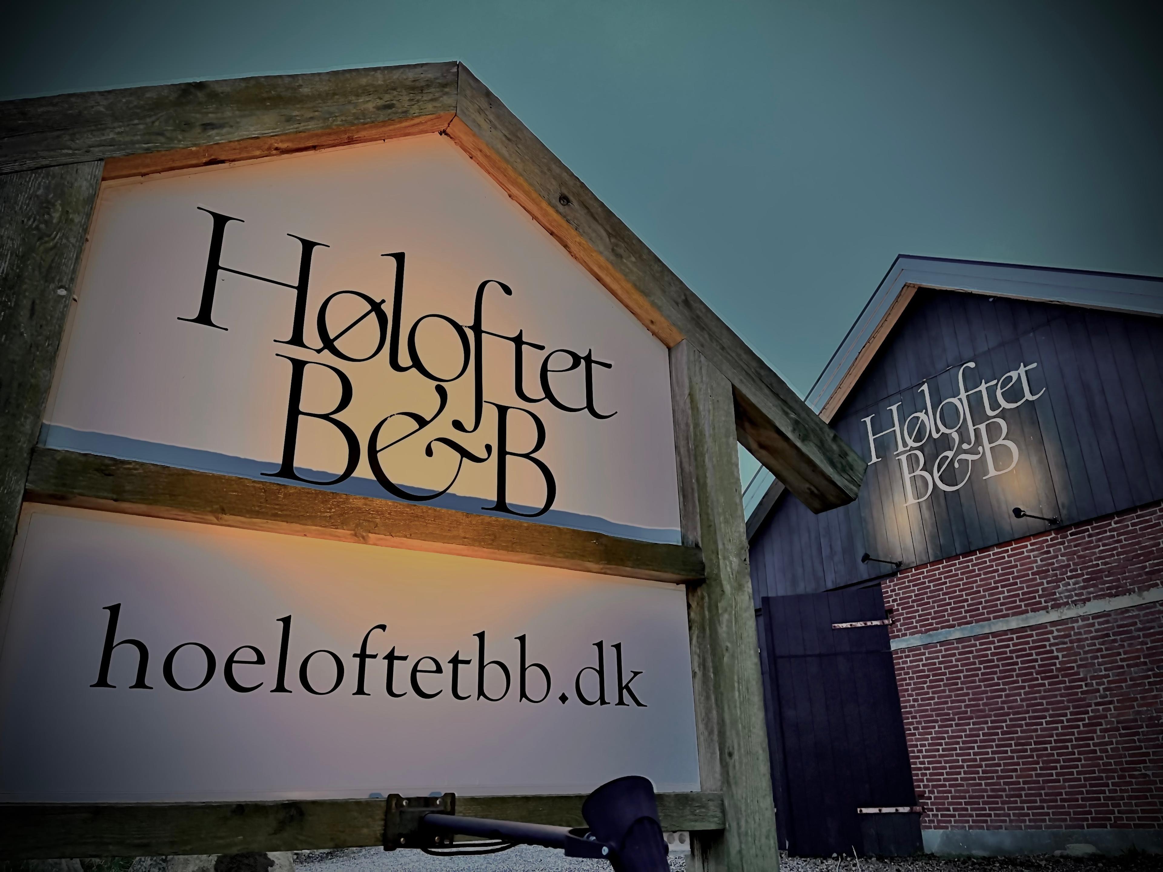 Skilt med navnet "Høloftet B&B" og webadressen "hoeloftetbb.dk" oplyst om aftenen.