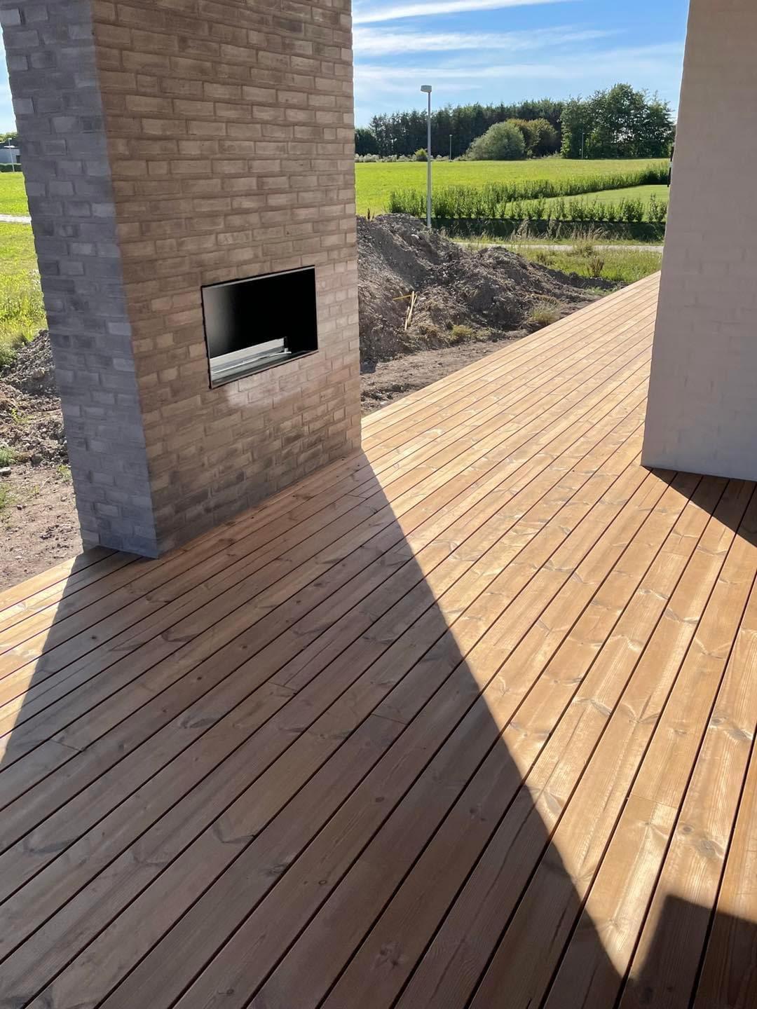 Terrasse med trædæk og murstensvæg, der fører til en grøn mark i baggrunden.