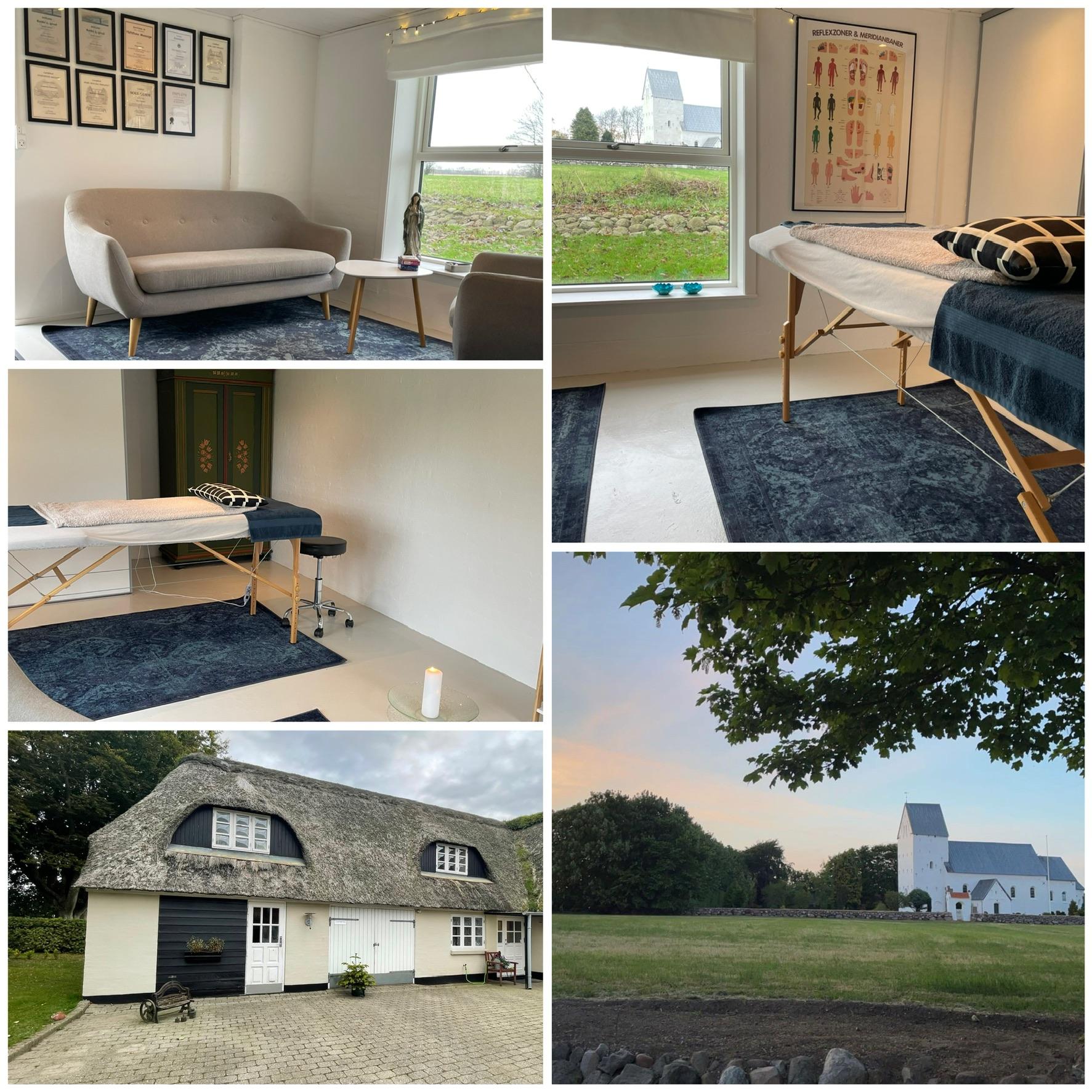 Stue med sofa, massagebord og udsigt til en gård og kirke i det danske landskab.