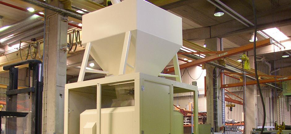 En stor hvid silo til opbevaring af materialer i en industriel hal med maskiner i baggrunden.