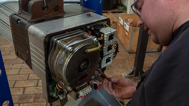En tekniker arbejder på en elektrisk motor, mens han justerer ledninger og komponenter i et værksted.