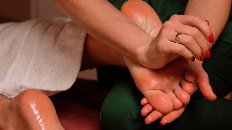 En person får fodmassage med en hånd, der masserer foden, mens den anden hånd holder om anklen.
