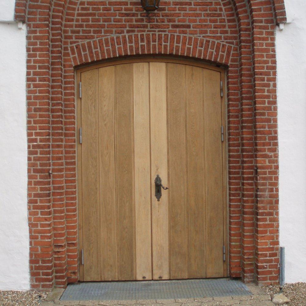 En stor, trædør med to paneler og en metalgreb, omgivet af mursten.