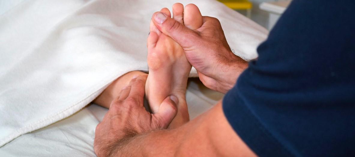 En person får fodmassage under et tæppe, hvor en hånd masserer foden.