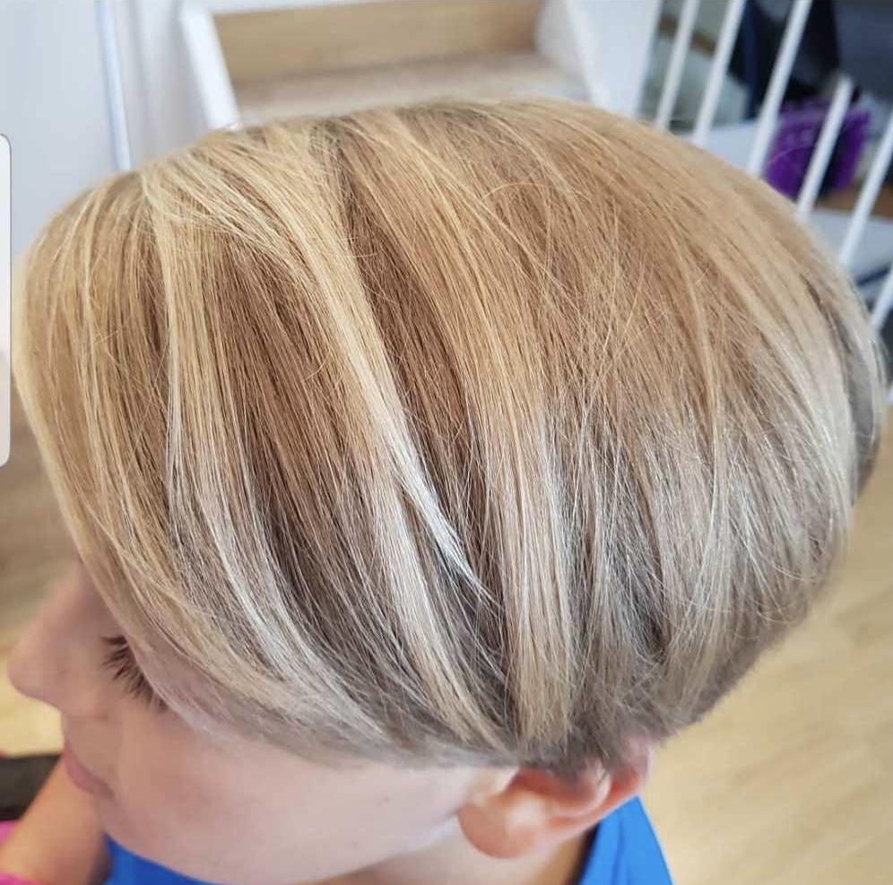 En dreng med kort, lyst hår med striber sidder i en frisørsalon.