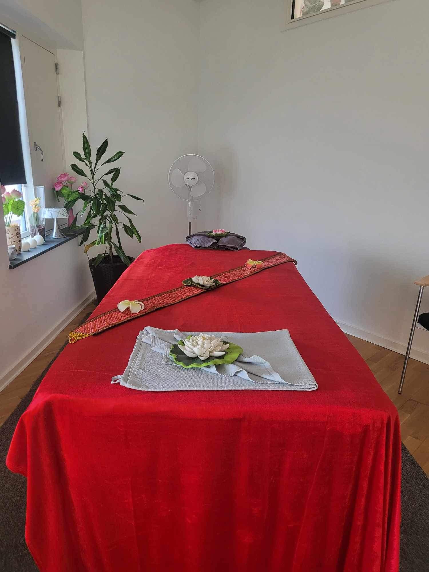 Et massagetæppe i rød farve med en lotusblomst og grønne blade på et bord i et lyst rum.