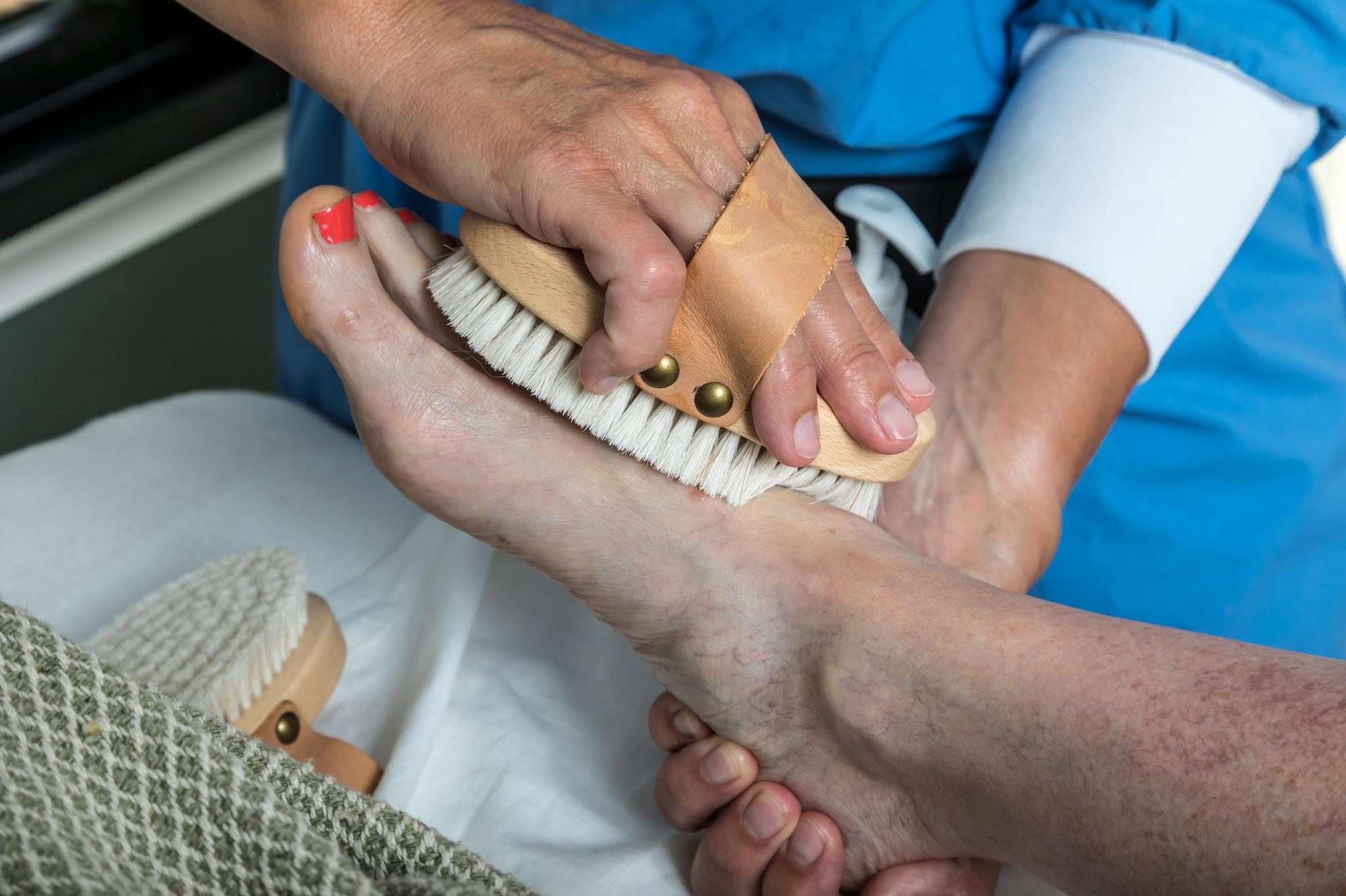 En person får en fodmassage med en børste, mens de ligger på en seng med en blød dyne.