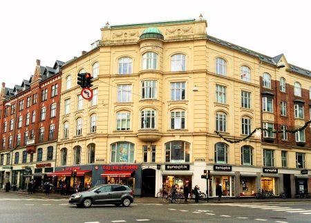 En smuk bygning i København med gule facader, butikker i stueetagen og trafiklys i forgrunden.