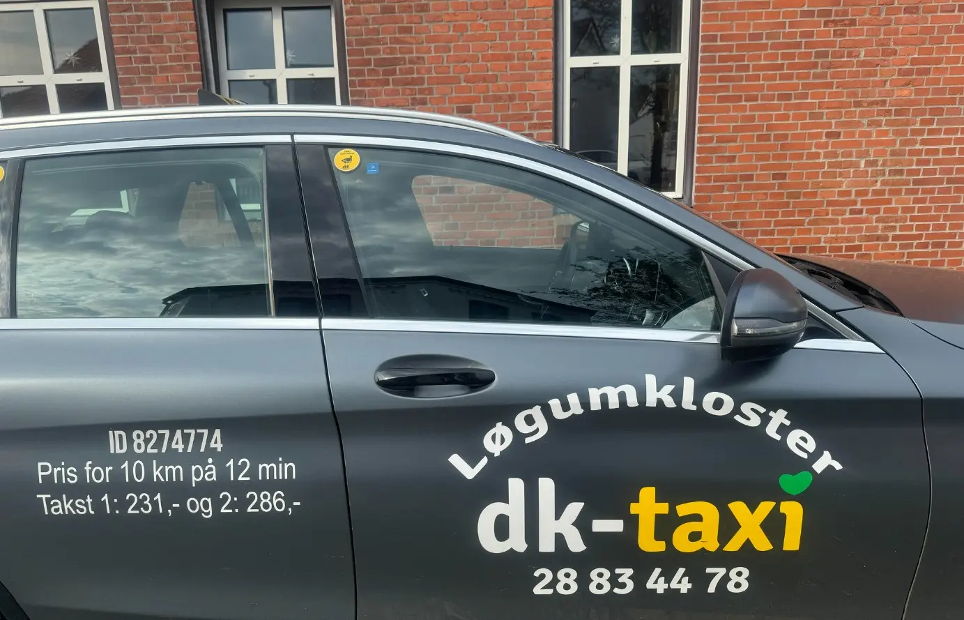 En taxi fra dk-taxi med teksten "Løgumkloster" og takstinformation på siden.