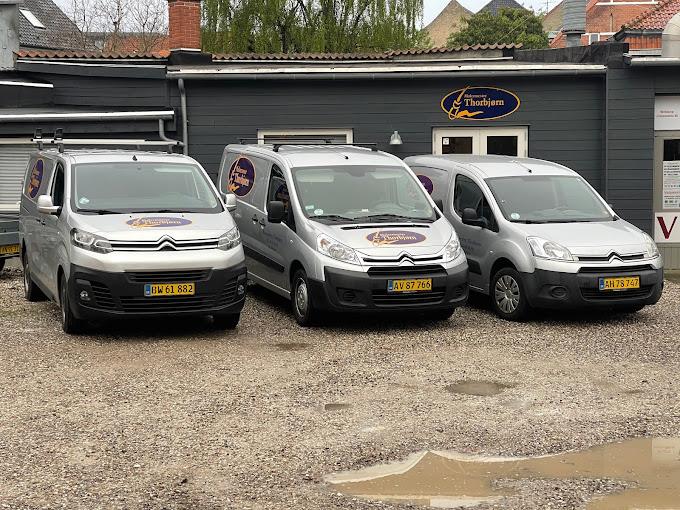 Tre sølvfarvede varevogne parkeret foran en bygning med et skilt, der viser virksomhedens navn.