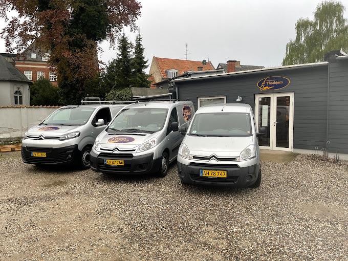 Tre sølvfarvede varevogne parkeret foran en grå bygning med logo og indgang.