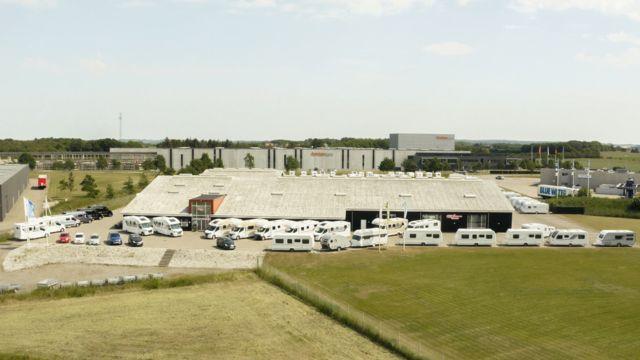 Oversigt over en campingvognsforhandler med mange campingvogne parkeret foran bygningen.