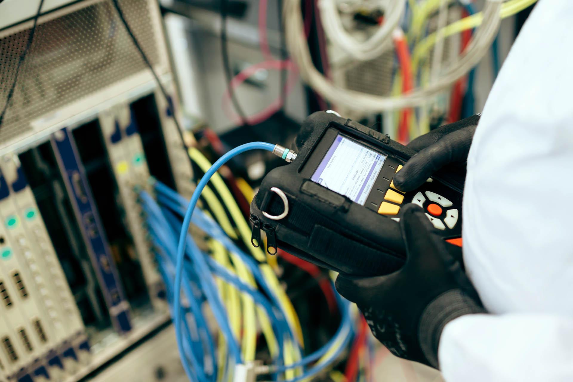En tekniker bruger en måleinstrument til at teste netværksforbindelser blandt farverige kabler.