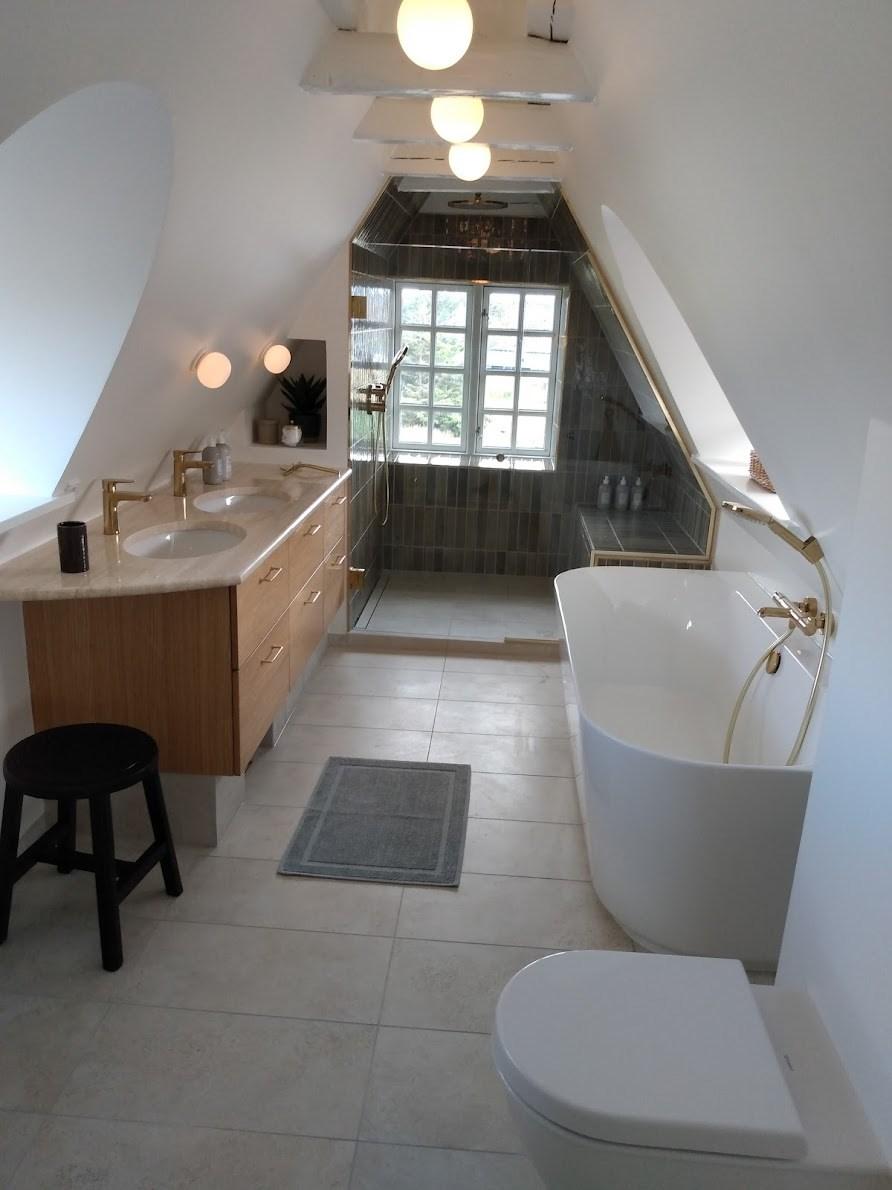 Moderne badeværelse med badekar, toilet, håndvask og store vinduer, belyst af loftlamper.