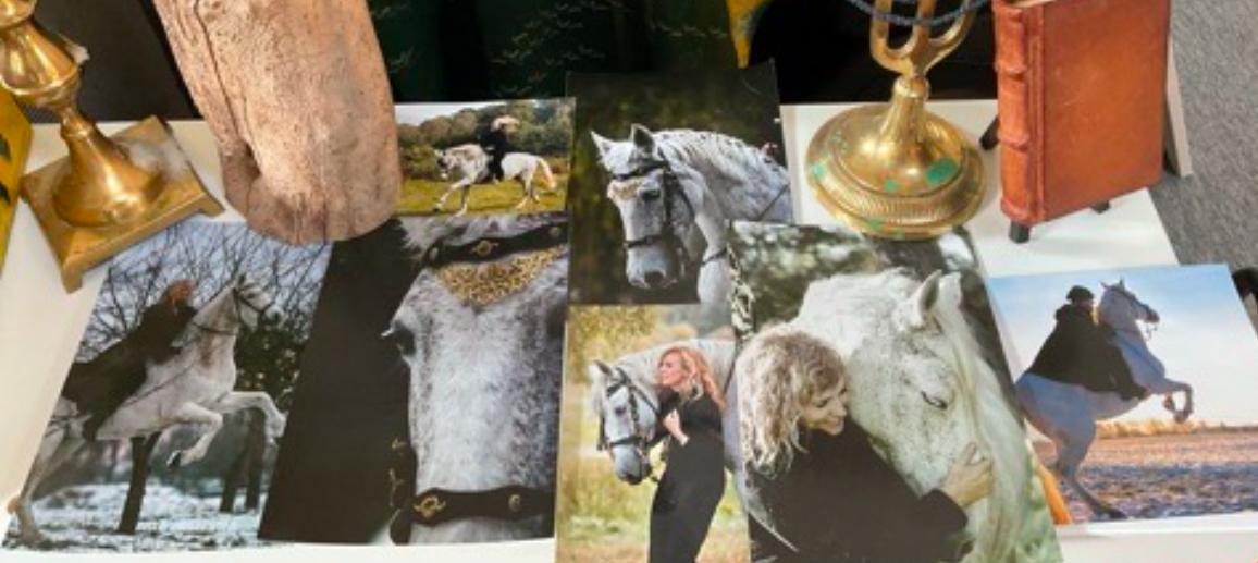 Billede af flere fotografier af heste, en lys lampe og en gammel bog på et bord.