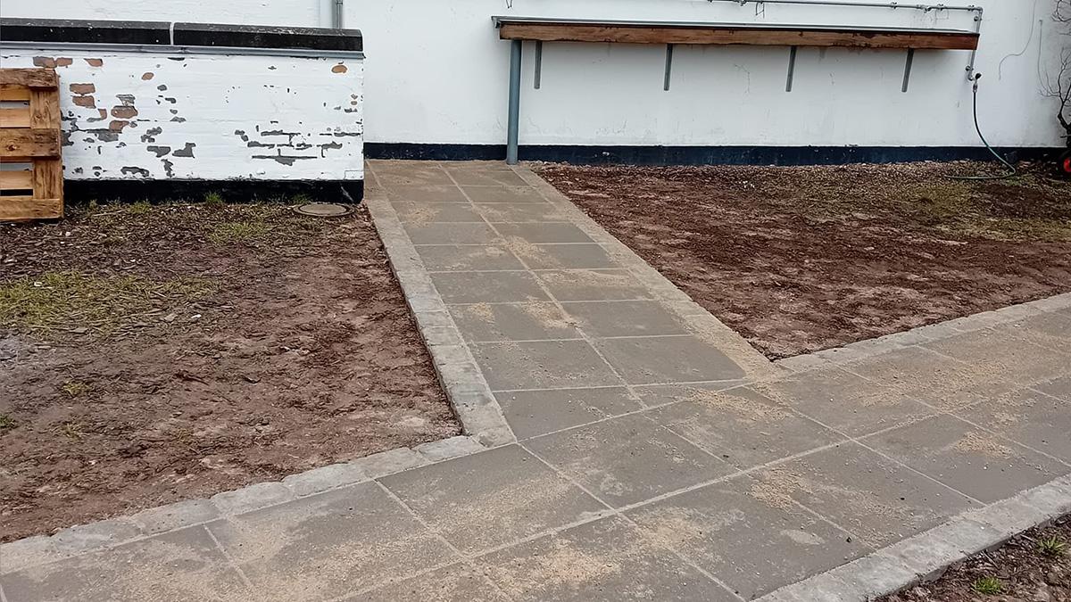 Nybelagt flisegang før beplantning, der fører til en væg med en træhylde.