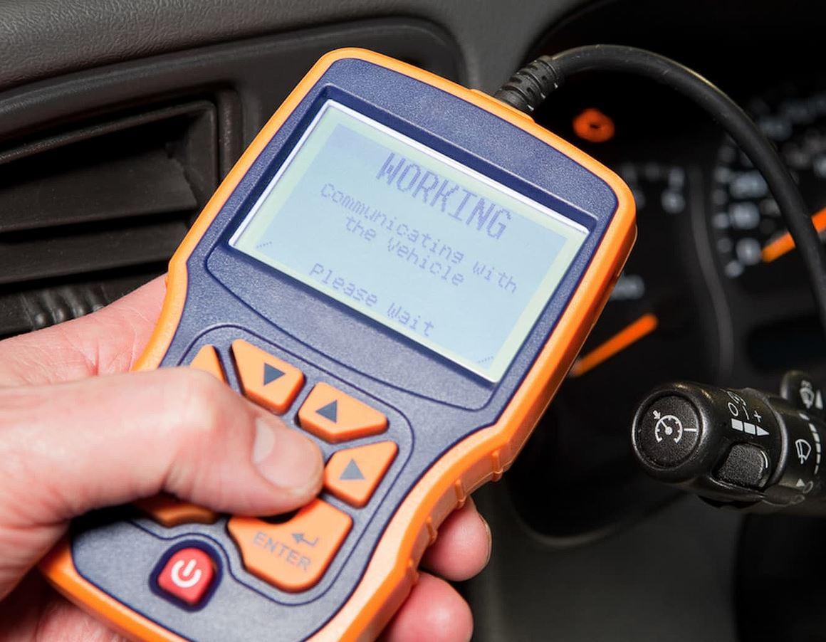 En hånd holder en bildiagnoseenhed, der viser "WORKING" på skærmen i en bils cockpit.