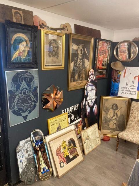 Væg med forskellige kunstværker, herunder malerier, rammer og skulpturer i en kunstnerisk indretning.
