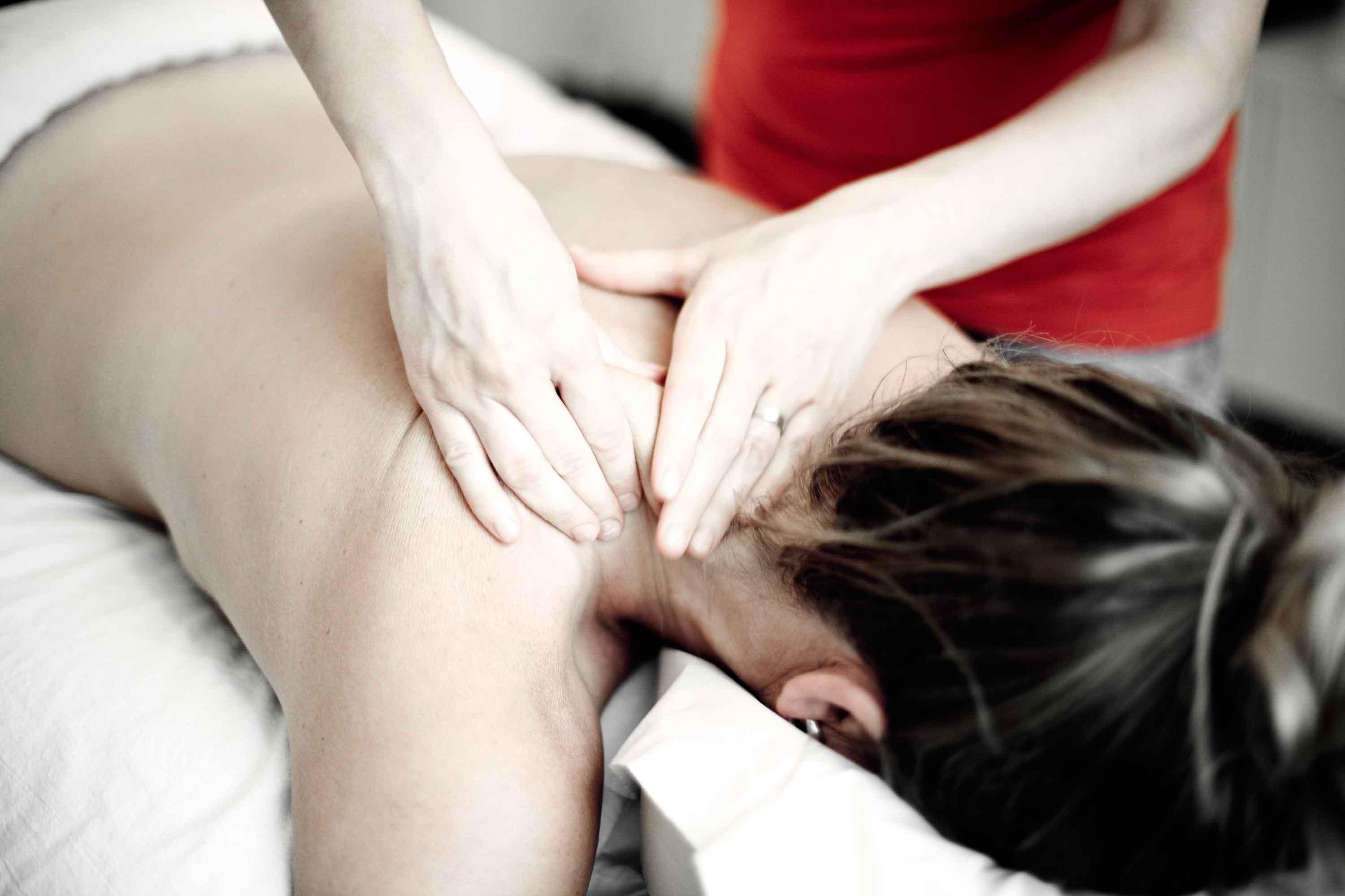 En kvinde får massage på ryggen, mens en behandler arbejder med hænderne på hendes skuldre.
