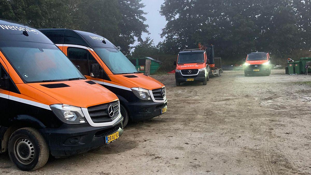 Tre Mercedes-varevogne med orange og sorte farver parkeret på en grusvej i skoven.