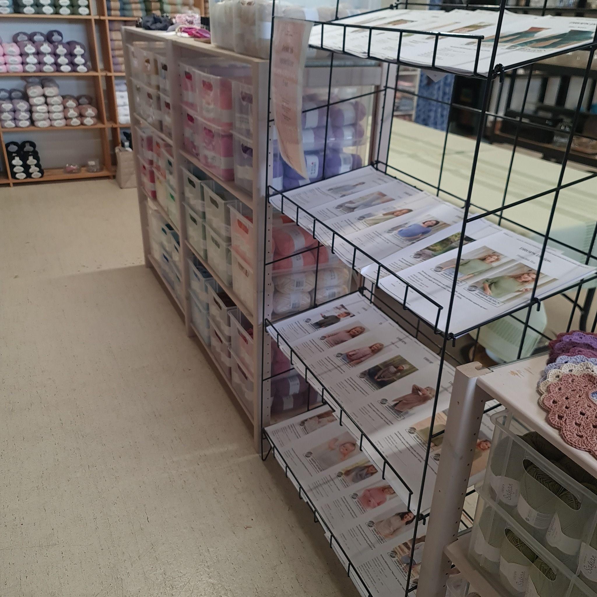 En butik med hylder fyldt med garn og opskrifter, der viser forskellige strikke- og hækleprojekter.