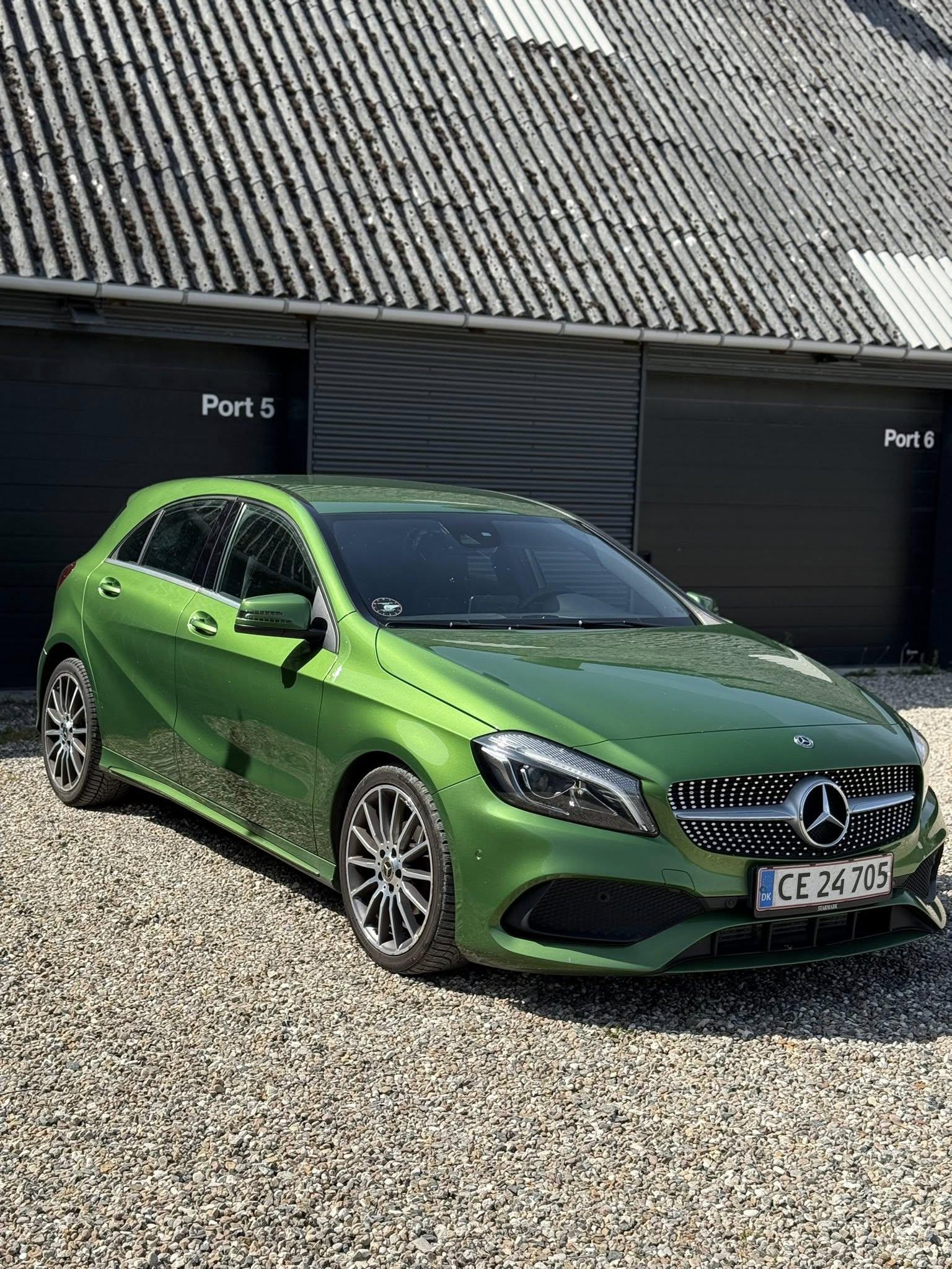 En grøn Mercedes A-klasse bil parkeret foran en bygning med sorte porte.
