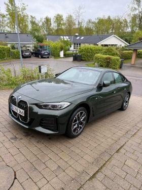 En grøn BMW 4-serie parkeret på en brostensbelagt vej i et boligområde med træer og huse i baggrunden.