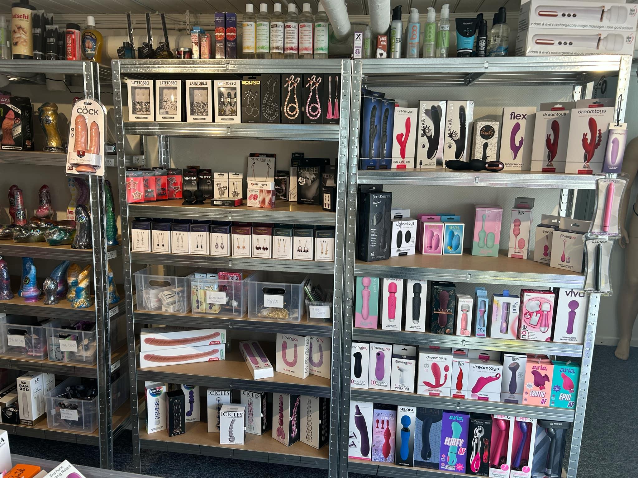 Butik med hylder fyldt med sexlegetøj og tilbehør i forskellige farver og former.