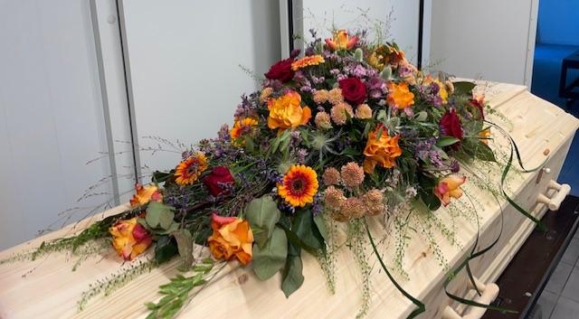 En smuk blomsterkrans i orange, rød og lilla nuancer ligger på en lys trækiste.