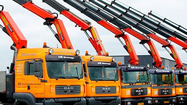 Flere orange lastbiler med kraner, der står parkeret i en række på en byggeplads.