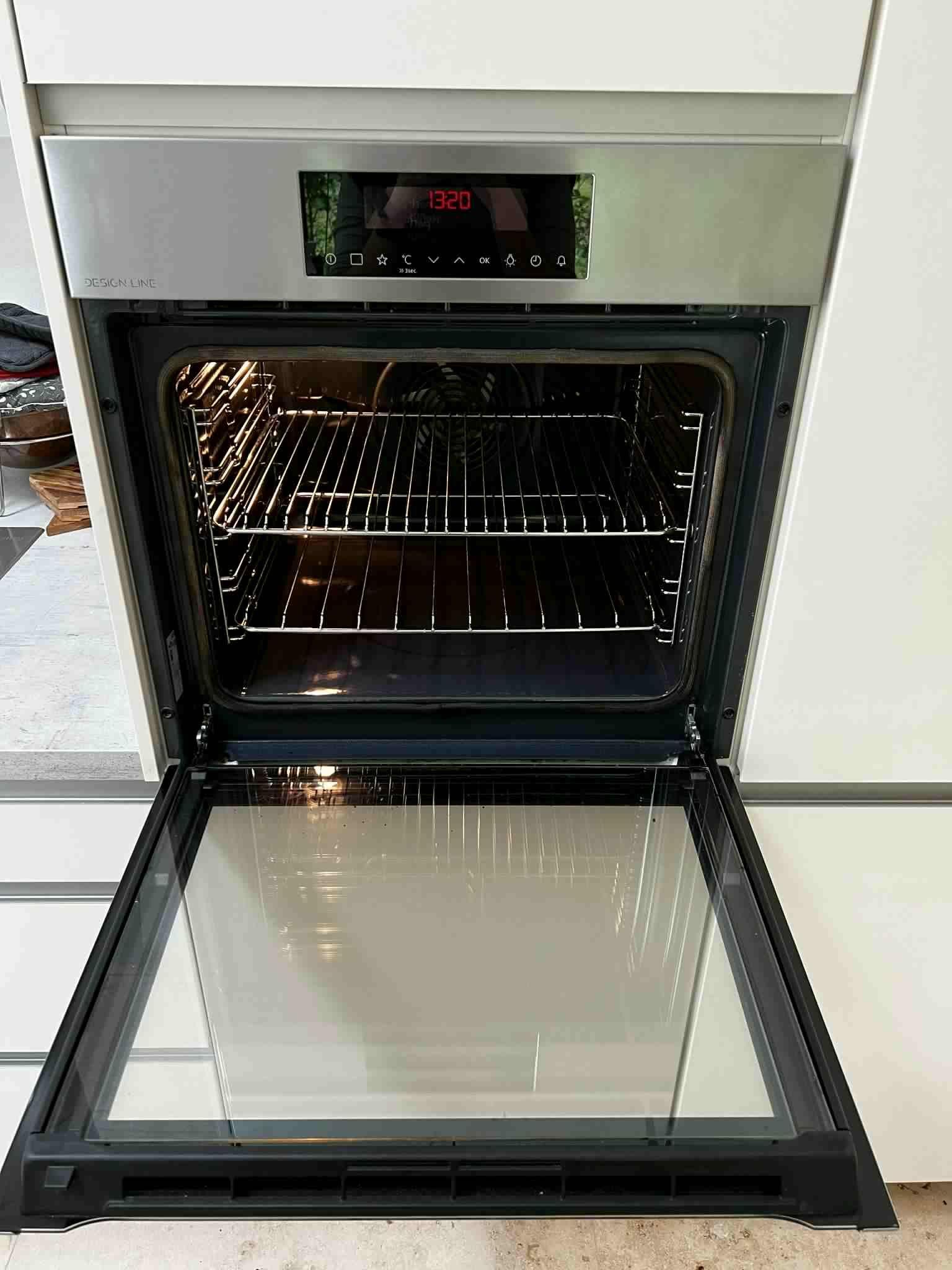 Indvendig visning af en moderne ovn med åbent glasdør og metalriste.