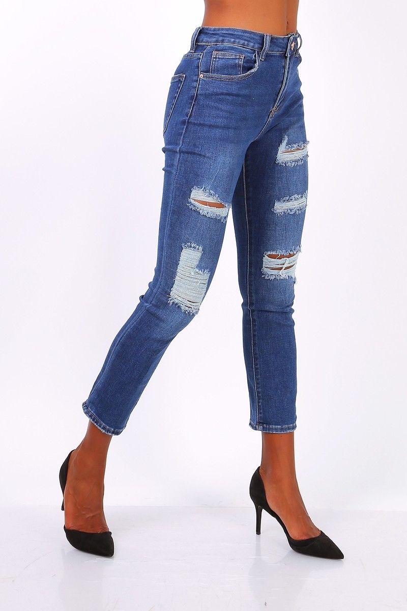 En person iført slidte jeans med huller og høje hæle, der står på en hvid baggrund.