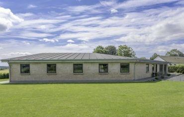 Moderne hus med fladt tag og store vinduer, beliggende på en grøn græsplæne under en blå himmel.